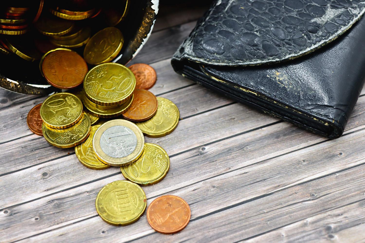 Monedes d'euro escampades amb una cartera vella, que representen la situació de vulnerabilitat econòmica.
